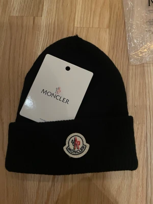 Svart mössa med logga  - Snygg svart ribbstickad mössa  med uppvikt kant och klassisk logga framtill. Perfekt accessoar för kyliga dagar och ger en clean streetwear-look. Tillverkad i mjukt material som sitter skönt på huvudet.