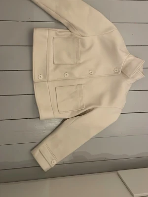Kräm vit jacka  - Kräm vit jacka med knappar. Passar perfekt till tidig vår. Knappen på höger arm är lite lös men det går att fixa enkelt. 