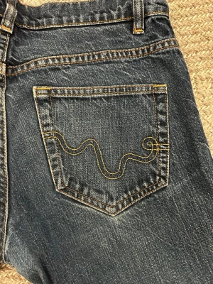 Mörkblå jeans från WESC - Säljer ett par mörkblå jeans från WESC med klassisk gul brodyr på bakfickorna och en gul etikett i midjan. Jeansen har normal passform och raka ben. Perfekta för dig som gillar stilrena detaljer och snygg tvätt. Dom är low waist. Dom kommer i 27W och 30L