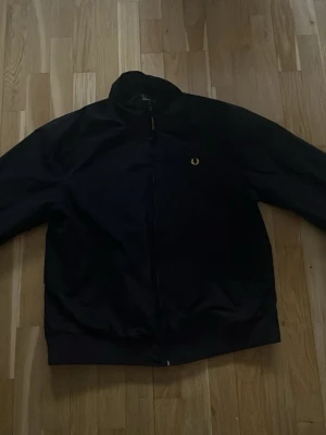 Svart vindjacka från Fred Perry - Svart vindjacka från Fred Perry. Använd fåtalet gånger då den inte passar mig. Storleken är XL men den passar även XXL.