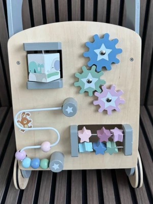 Gåvagn i trä med aktivitetsleksaker - Säljer en söt gåvagn i trä med flera aktivitetsleksaker på framsidan, som kugghjul, snurrande klossar, stjärnor och kulbana. Färgerna är pastellblå, mintgrön, lila, rosa och natur. Perfekt för små barn som vill lära sig gå och leka samtidigt.