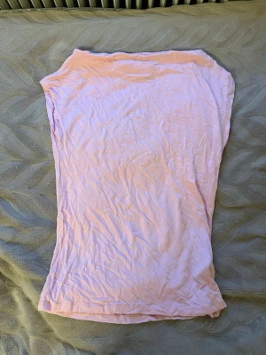 Ljusrosa axelbandslös tubtopp - Säljer en ljusrosa tubtopp i mjuk bomull. Toppen är axelbandslös och har en enkel, rak form som sitter snyggt mot kroppen. Perfekt att styla med jeans eller kjol för en chill look. Färgen är söt och passar bra till vår och sommar.