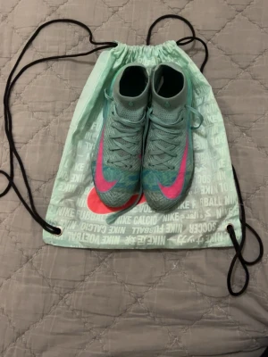 Nike Mercurial fotbollsskor turkos/rosa elite - Säljer ett par Nike Mercurial fotbollsskor i turkos med stora rosa swoosh-loggor och coola detaljer i gult och svart på sulan. Skorna har snörning, högre strumpkrage och är tillverkade i syntetmaterial för bästa känsla på planen. Perfekta för dig som vill sticka ut! Elites.