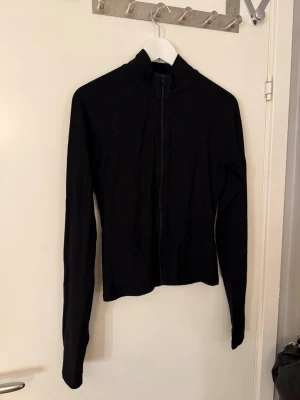 Svart ziptröja från Gina Tricot - Säljer en svart långärmad ziptröja från Gina Tricot i storlek L. Tröjan har hög krage, tumhål i ärmsluten och är gjord i mjuk bomull. Perfekt till lager på lager och enkel att matcha med allt.