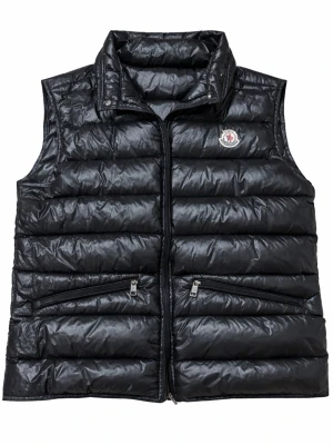 Svart dunväst från Moncler - Säljer en svart dunväst från Moncler  med quiltad design och hög krage. Västen har två snedställda fickor med dragkedja och ett Moncler-emblem på bröstet. Perfekt för lager-på-lager och snygg till streetwear. Hör gärna av er vid frågor