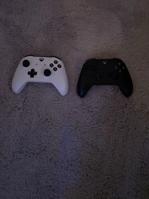 Xbox Series Wireless Controller (vit & svart) - Säljer två Xbox Series trådlösa handkontroller, en vit och en svart. Båda har klassisk Xbox-design med responsiva knappar och joysticks. Kontrollerna är i gott skick utan synligt slitage eller defekter. Perfekt för spel på Xbox eller PC. Y på den svarta fastnar ibland men den funkar. Batterier följer med.