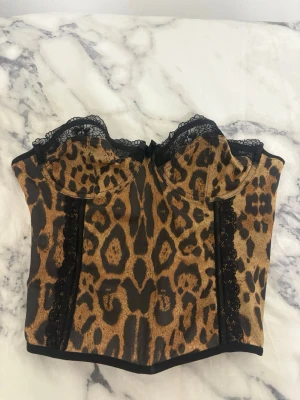 Leopardmönstrad korsett från Romwe - Säljer en snygg leopardmönstrad korsett från Romwe i storlek S. Toppen har svarta spetsdetaljer upptill och hakknäppning bak. Materialet är lätt och meshigt med svarta paneler på sidorna. Perfekt för dig som vill sticka ut med djurmönster.