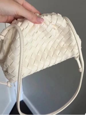 Beige flätad axelväska i skinn - Säljer en beige axelväska med snyggt flätat mönster och rundad form. Väskan har en lång axelrem och är tillverkad i skinn, vilket ger en lyxig känsla. Perfekt för dig som gillar stilrena accessoarer med lite extra detalj.