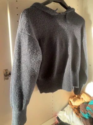 Mörkblå  hoodie i stickad ullmix - Mysig mörkblå  hoodie med huva och långa ärmar. Tröjan är stickad i ett fluffigt ullmix-material och har en relaxed passform. Perfekt för kyliga dagar när du vill vara både bekväm och snygg.