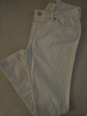 ZARA Vita Z1975 Denim jeans - Snygga vita jeans från ZARA Z1975 Denim med klassisk femficksdesign. Byxorna har låg midja, silverfärgade nitar och knapp, samt bälteshällor. Materialet är mjuk bomull med stretch för extra komfort.