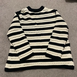 Randig stickad tröja från H&M Mama - Säljer en svart och vit stickad tröja från H&M Mama i storlek S. Tröjan har breda ränder och ett hålmönster som ger en cool och unik look. Den har långärmade och en ribbad krage som sitter skönt runt halsen. Perfekt för dig som gillar stickade plagg med lite extra detaljer.