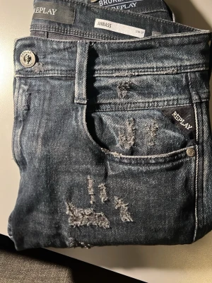 Replay Anbass  slitna jeans - Säljer ett par Replay Anbass jeans i mörk naturlig tvätt med slitningar och trasiga detaljer på benen. Slim fit-modell ny pris ligger runt 3000, hör av dig om funderingar eller fler bilder. Storlek 28/32. Knappt använda 