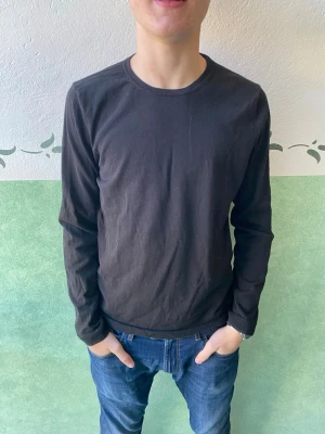 Svart långärmad tröja Riley - En stilren svart långärmad tröja från Riley. Tröjan har rund halsringning och är gjord i ett mjukt material som känns skönt mot huden. Passformen är normal och den är enkel att matcha med olika outfits.