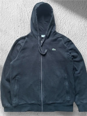 Svart Lacoste Zip Hoodie  - Klassisk Lacoste hoodie i svart färg. Tröjan är i mycket bra skick. Sparsamt använd :-)         Storlek: M.                                                             Skick: Mycket bra skick!                    Färg: Svart                                                          Märke: Lacoste                                                   Modell: Hoodie med dragkedja                           Hör gärna av dig vid frågor så svarar jag så fort jag kan! 😁   