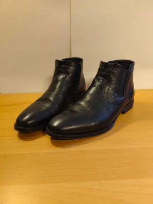 Svarta  boots i skinn - 42 - Ny.  - Säljer ett par svarta boots, Skor Perfekta för dig som gillar stilrena och klassiska boots. Enligt bild, använd bara en gång. Storlek 42.