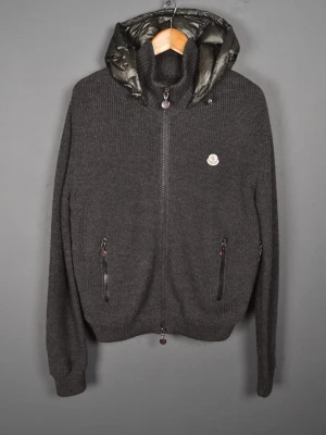 Mörkgrå stickad jacka från Moncler - Säljer en stilren Moncler jacka i grön färg med dunfodrad huva. Perfekt för höst/vår eller mild vinter. Väldigt snygg kombination av stickat material och dun som ger både värme och stil.  🔹 Original Moncler 🔹 Bekväm passform 🔹 Fint skick, sparsamt använd 🔹 Dragkedjor och detaljer i bra skick  Säljer pga att den inte kommer till användning. Pris kan diskuteras vid snabb affär 💸 Skicka gärna meddelande om du vill ha fler bilder eller mått!