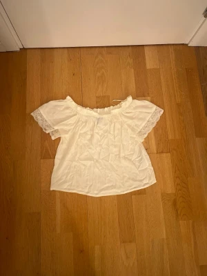 Vit offshoulder blus från Vero Moda - Säljer en söt vit offshoulder blus från Vero Moda i storlek XS. Blusen har korta ärmar med spetsdetaljer och en luftig, lätt struktur. Perfekt för varma dagar.