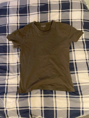 Olivgrön t-shirt från Kappahl - En enkel olivgrön t-shirt från Kappahl i storlek S. Klassisk rund halsringning och korta ärmar. Tillverkad i mjuk bomull som känns skön mot huden. Perfekt basplagg att ha i garderoben.