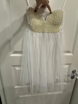 Vit pärlbeströdd kortklänning Reverse - En vit kortklänning från Reverse med axelbandslös design och pärlbeströdd överdel. 