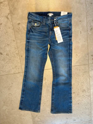 Chunky low flare jeans från Gina Tricot - Chunky low flare jeans från Gina Tricot i mid blue. Modellen har låg midja, klassiska fem fickor och snygga knappdetaljer på bakfickorna. Jeansen har en flare passform med lite bredare ben och är tillverkade i slitstark denim av bomull.