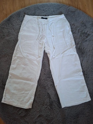 Vita korta linnebyxor från Estelle, strl 40 - Snygga vita korta  linnebyxor från Estelle i storlek 40. Byxorna har breda ben, snörning i midjan och stora fickor både fram och bak. Perfekta för en chill och fräsch look under varma dagar. Materialet är linne som ger en skön och luftig känsla.