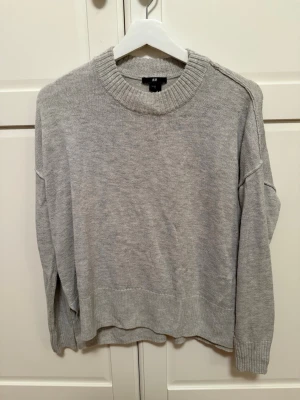 Grå stickad tröja - Mysig grå tunnstickad tröja från H&M i storlek XS. Tröjan har en rund hals med bred ribbad kant och långa ärmar. 