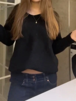 Svart stickad tröja med lång ärm - En svart stickad tröja med rund hals och långa ärmar. Tröjan har en loose passform och är lite croppad, vilket gör att den slutar precis ovanför midjan. Perfekt att matcha med jeans för en enkel och stilren look.