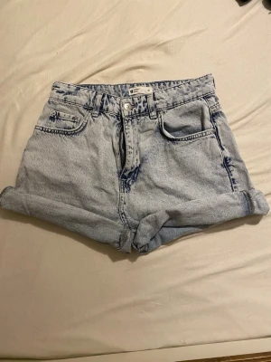 Ljusblå jeansshorts från Perfect Jeans - Säljer ett par ljusblå jeansshorts från Perfect Jeans i storlek 36. De är högmidjade med klassisk femficksdesign, uppvikta ben och tydliga blå tvättade detaljer. Perfekt för dig som gillar retrovibe och vill ha en chill look.