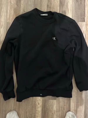 Svart sweatshirt från Calvin Klein Jeans - Svart sweatshirt från Calvin Klein. Tröjan har rund hals, ribbade muddar och är långärmad. Materialet är mjukt och känns skönt mot huden, perfekt för chill dagar. Passformen är normal och enkel att matcha med jeans eller joggers. Pris går att diskuteras 