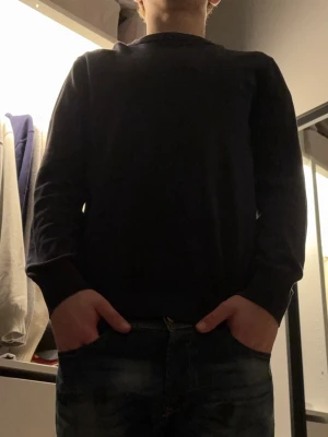 Mörkblå stickad tröja med rund hals - Snygg mörkblå stickad tröja med rund hals och långa ärmar. Enkel och stilren design som passar perfekt till jeans eller chinos. Mjuk och skön kvalitet, perfekt för kyliga dagar. Tröjan har en normal passform och ribbade muddar vid ärmslut och nederkant.