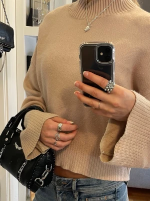 Beige stickad tröja - Beige stickad tröja med breda, långa ärmar och ribbade muddar vid ärmslut, halsringning och nederkant. Skulle säga är en S men passar XS och M också! 