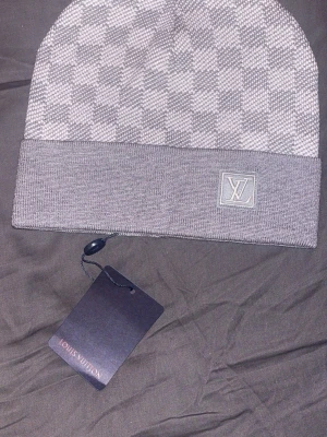 Grå rutig mössa  - Snygg grå mössa från  med klassiskt rutigt mönster och uppvikt Mössan är stickad och har en exklusiv vibe som passar perfekt till streetwear och lyxiga outfits.