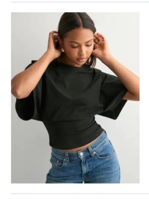 Svart croppad topp med vida ärmar - Snygg svart croppad topp med bred midja och vida korta ärmar. Toppen har en stilren och modern look som passar perfekt till jeans eller kjol. Materialet känns mjukt och följsamt mot kroppen och ger en cool siluett.