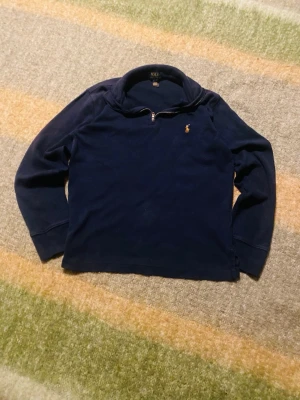 Marinblå half zip tröja Polo Ralph Lauren - Säljer en marinblå långärmad tröja från Polo Ralph Lauren med half zip och klassisk krage. Tröjan har det ikoniska broderade logot på bröstet och är gjord i mjuk bomull. Perfekt för chill dagar och snygg till jeans.  10-12 år! Säljs i befintligt skick