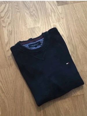 Svart tröja Tommy Hilfiger Sport S - Svart långärmad tröja från Tommy Hilfiger Sport i storlek S. Klassisk rund hals med ribbade muddar och nederkant. Liten broderad logga på bröstet i rött, vitt och blått. Perfekt för dig som gillar stilrena och enkla plagg.