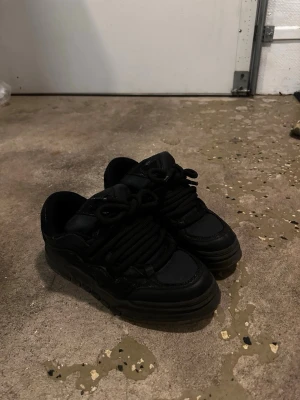 Svarta Bershka chunky sneakers med snörning  - Säljer ett par svarta chunky sneakers med breda svarta skosnören och rund tå. Skorna har en tjock platt sula och är tillverkade i en mix av syntet och skinnmaterial. Perfekta för dig som gillar streetstyle och vill ha en cool look.