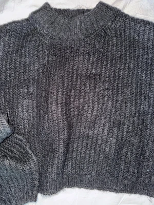 Mörkgrå stickad tröja - Säljer en mörkgrå stickad tröja med ribbad struktur och hög krage. Tröjan har en loose passform och är perfekt för kyliga dagar. Materialet är mjukt och ger en mysig känsla. Passar dig som gillar enkel och stilren design. Den är croppad.