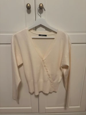  kofta från Gina Tricot - Säljer en mjuk och stilren beige kofta från Gina Tricot med v-ringning och knappar framtill. Koftan har långärmad design. Materialet känns skönt mot huden och passar till många olika outfits. Använd 2 gånger 