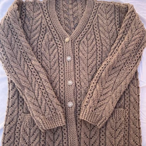 Handstickad brun Ulltröja med Fickor – Mjuk, Varm  - En vacker handstickad brun tröja, gjord med kärlek och omsorg av mjuk ull av hög kvalitet. Tröjan har ett fint bladmönster, två fickor framtill, och extra knappar sydda inuti om någon skulle tappas bort. Den är helt ny och oanvänd, mycket bekväm och varm, och passar perfekt både till vardags och som gåva till någon du tycker om.  Perfekt present till jul, födelsedag eller vinterbruk – en unik och mysig tröja för kalla dagar!  Detaljer: 	•	Material: 100 % mjuk ull 	•	Skick: Ny / Oanvänd 	•	Handgj