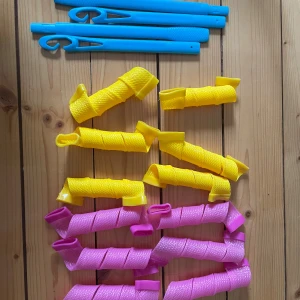 Spiral hårspolar med krokar - Färgglada spiral hårspolar i gult och rosa, inklusive fyra blå krokar för enkel applicering. Perfekt för att skapa lockar utan värme. Alla delar ser ut att vara i mycket gott skick, utan synligt slitage eller defekter. Använda fåtal gånger 