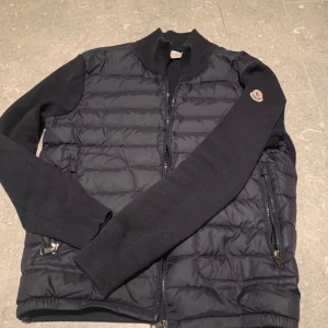Mörkblå cardigan  från Moncler - Säljer en snygg mörkblå cardigan från Moncler med quiltad design och dragkedja. Jackan har långa ärmar och en ribbad krage. Perfekt för kyligare dagar. Säljer eftersom att den inte passar längre. 