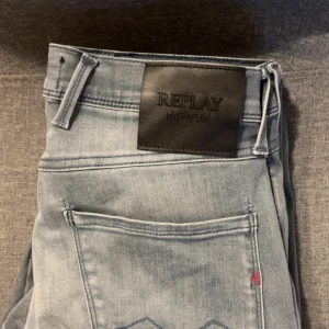Ljusblå Replay Hyperflex jeans - Säljer ett par ljusblå Replay anbass jeans med klassisk femficksdesign och svarta läderpatch bak i midjan. Jeansen har en modern passform och är tillverkade i stretchigt material för extra komfort. Storleken är W28 L30.