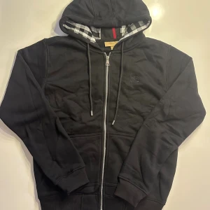 Svart Burberry kofta zip M - En svart burberry zip i storlek M, kan troligtvis passa en S också. Väldigt fint skick! Enda problemet är att tagen vid nacken där det ska stå burberry har gått bort i tvätten. Men det är inget någon märker när man har på sig den 😊 Kolla gärna in min profil för mer!