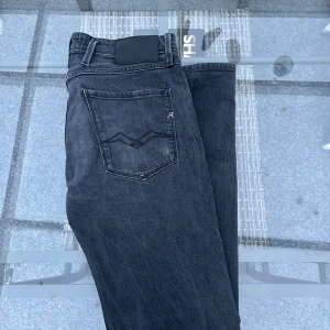 Replay Anbass Slim Fit Jeans – Svartgrå, stl 31 - Snygga jeans från Replay, modell Anbass Slim Fit i storlek 31. Mjuk och stretchig denim i en snygg svartgrå tvätt med lätt slitna detaljer. Klassisk design med Replay-logga på bakfickan och läderpatch bak i midjan. Superskön passform som sitter perfekt utan att bli för tighta.  I riktigt fint skick – sparsamt använda, inga märken eller hål. Perfekta både till vardags och när du vill klä upp dig lite mer.  📏 Storlek: 31 🎨 Färg: Svartgrå 👖 Modell: Replay Anbass (Slim Fit) 🧵 Skick: Mycket bra 