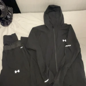Svarta mjukisbyxor från Under Armour - Svarta mjukisbyxor från Under Armour med elastisk midja och logga på benet. Byxorna är i mjukt material och har en avslappnad passform, perfekta för träning eller chill. Snygg och enkel design med diskreta detaljer.