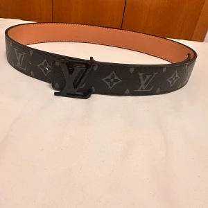 Svart  skärp i skinn - Svart bälte i skinn med klassiskt monogrammönster och s i svart metall. Insidan är beige med snygga sömmar och märkning 'made in France'. Perfekt accessoar för att lyfta din outfit.