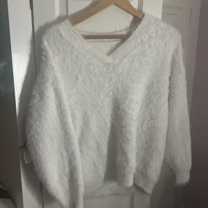 Vit fluffig stickad tröja v-ringad - Supermjuk och fluffig vit stickad tröja med v-ringad hals och långa ärmar. Tröjan har en oversized känsla och ribbade muddar vid hals, ärmslut och nederkant. Perfekt för att mysa i under kyliga dagar. Den här tröjan är så fluffig och snygg, jag använt 3 gånger och den hänger i min garderob och inte kommit till användning‼️ Den här tröjan behöver ett nytt hem och den är väldigt skön och mysig att ha på sig 🥰🥰