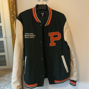 Basket collagejacka - Oanvänd  - Köpt i staden philly.  en collegeinspirerad bomberjacka från FSBN med svart kropp och vita ärmar. Jackan har stora broderade patches i orange och vitt, ribbade muddar med orange och svart ränder, samt tryckknappar framtill. Materialmix av ull och skinn, perfekt för dig som gillar sportig stil.