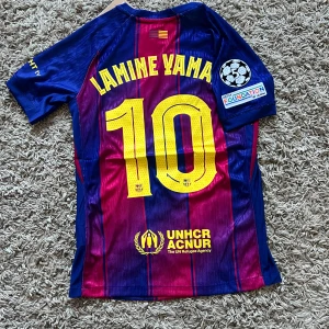 FC Barcelona Lamine Yamal tröja Nike small - Säljer en FC Barcelona matchtröja med Lamine Yamal och nummer 10 på ryggen. Tröjan är kortärmad, har blå och vinröda ränder, gula detaljer och klubbmärke framtill. Tillverkad i lätt Dri-FIT material, officiell Nike-produkt med Champions League-märke på ärmen. Spelar version
