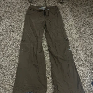 Bruna byxor från Roxy Girl - Bruna byxor från Roxy Girl med vida/bootcut ben och cargofickor på sidorna. Byxorna har meshfoder i ljusblått och är i täck-matterial.